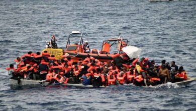 Overcrowded migrant boat at sea with people wearing life jackets as rescue team approaches in a realistic ocean setting
