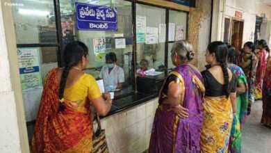 Patients standing in queue at a hospital service counter under NTR Vaidya Seva scheme interacting with staff behind a glass partition