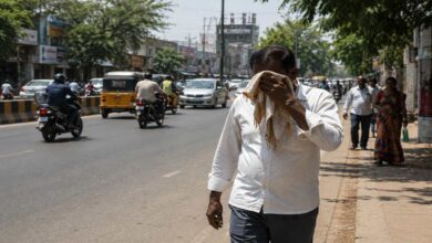 People walking on a busy Telangana road during extreme heatwave conditions under strong summer sunlight.